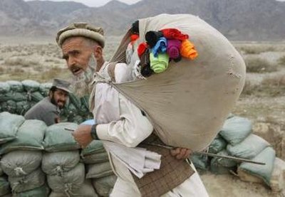 A man carries his belongings as he walks past a policeman on duty near Peshad village, Kunar Province, eastern Afghanistan February 19, 2009. REUTERS/Oleg Popov (AFGHANISTAN)