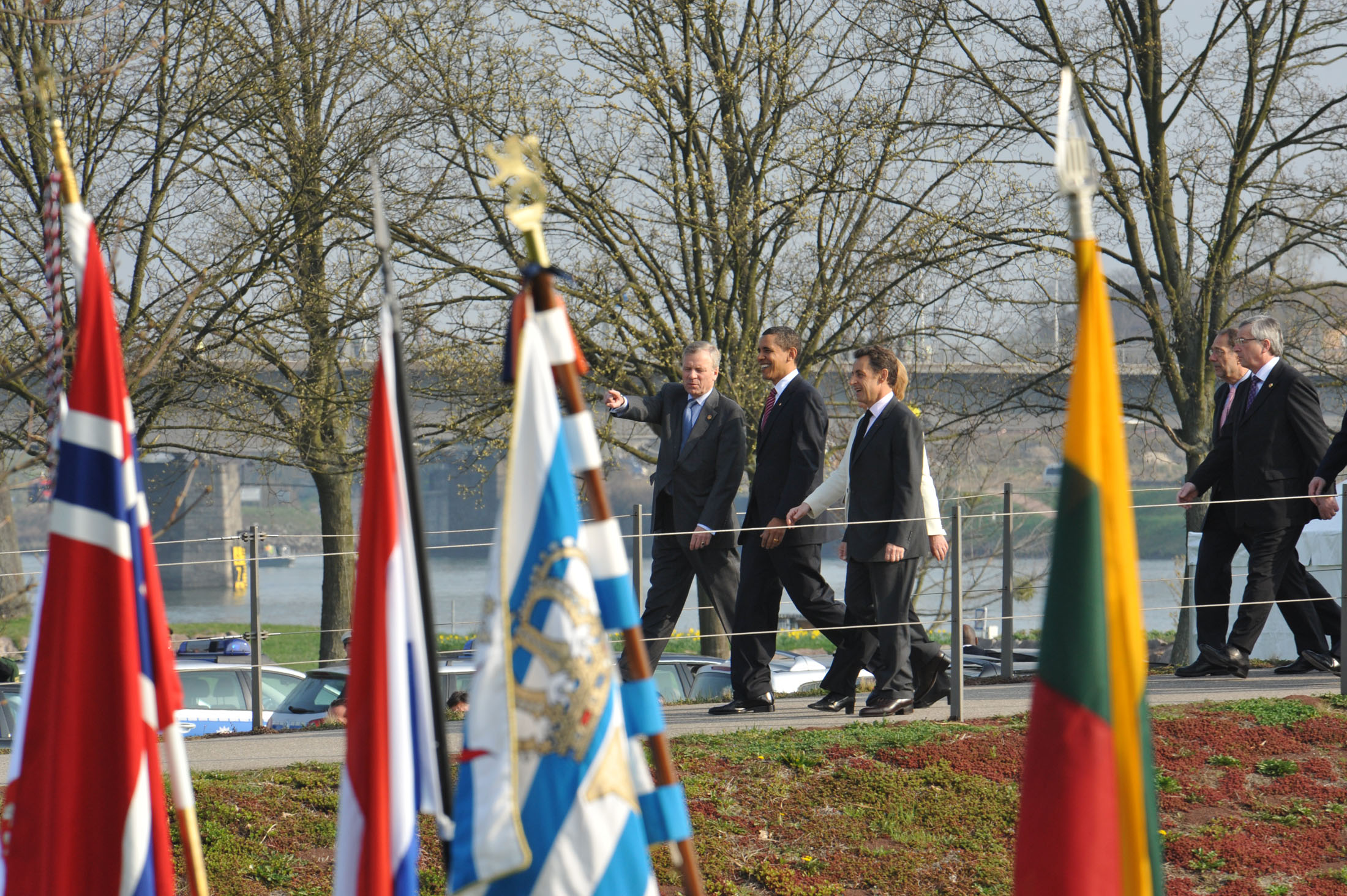 NATO Secretary Jaap de Hoop Scheffer, Barack H. Obama, President of the United States of America, Nicolas Sarkozy, President of France, and Angela Merkel, Chancellor of the Federal Republic of Germany (hidden by Sarkozy) crossing the "Passerelle de deux rives" from Germany into France (NATO photo, 4 April 2009)